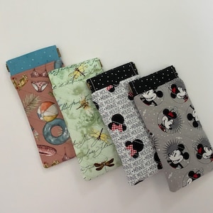 May include: Four rectangular fabric cases for glasses or small items. The first is pink with beach icons, the second is light green with dragonfly illustrations, the third is white with black Minnie Mouse text, and the fourth is gray with Minnie Mouse faces.