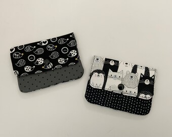 May include: Two black and white fabric coin purses with a button closure. One purse has a pattern of fish and the other has a pattern of animals.