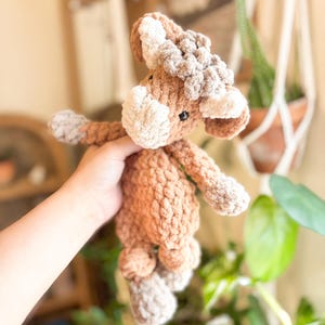 May include: A handmade crochet horse toy in shades of brown and beige. The plush toy features a textured body, a fluffy mane, and small black eyes. The horse has outstretched arms and legs, giving it a playful appearance. A soft and cuddly toy for children.