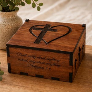 May include: A rectangular wooden box with a dark brown finish featuring a laser-engraved heart and cross on the lid. The front panel is inscribed with the text: Don't worry about anything; instead, pray about everything. Philippians 4:6.