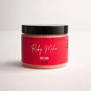 May include: A clear jar of Ruby Melon Body Scrub with a black lid. The jar has a red label with white script that reads "Ruby Melon" and "Body Scrub". The jar contains a pinkish scrub and is 8 oz (226g).