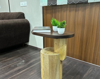 May include: A wooden side table with a rounded top and a cylindrical base. The table has a light brown finish and is decorated with a series of vertical grooves. Two small potted plants are on the table.