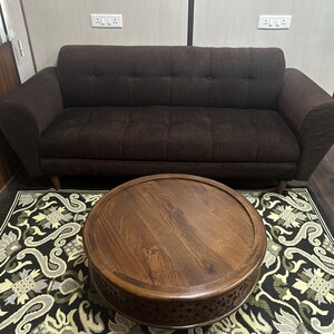May include: A dark brown sofa with a round wooden coffee table with intricate carvings. The table is on a black and white patterned rug.