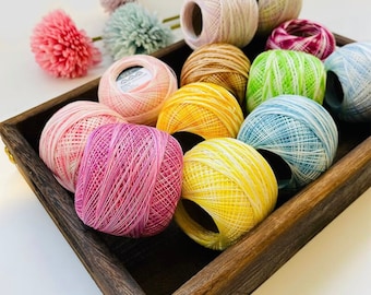 May include: A wooden box filled with colorful balls of yarn. The yarn is in shades of pink, red, yellow, green, blue, and white. The yarn is arranged in a circular pattern.