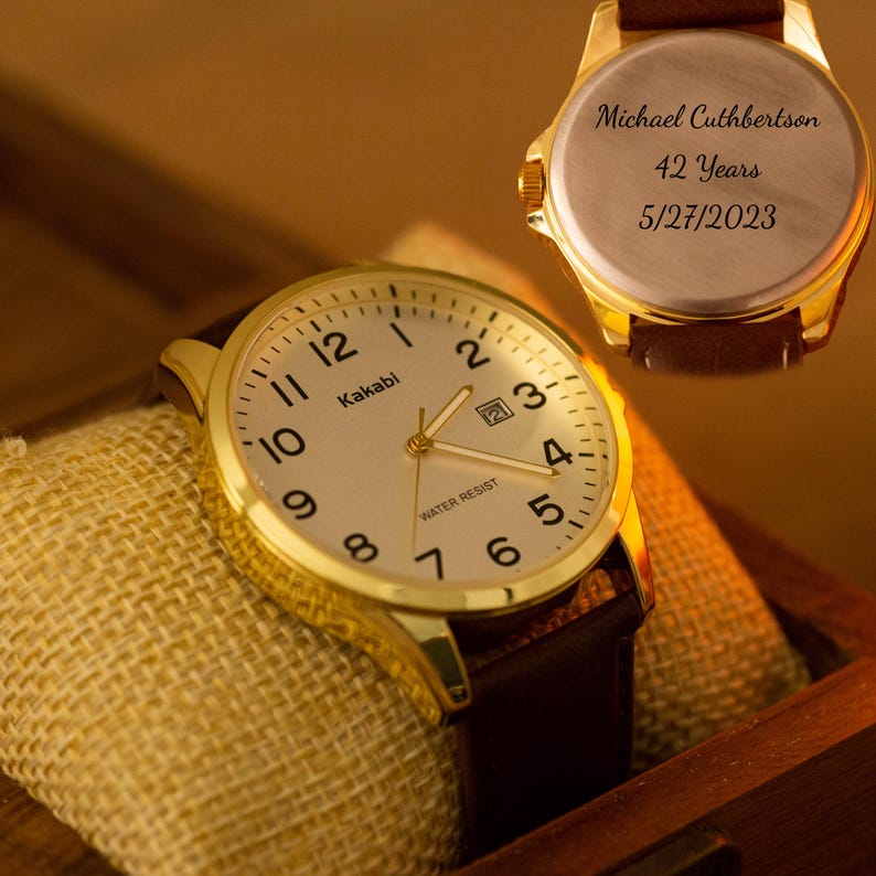 Puede incluir: Un reloj de pulsera Kakabi dorado con una correa de cuero marr&oacute;n. La esfera del reloj tiene n&uacute;meros y agujas negros. La parte trasera del reloj est&aacute; grabada con "Michael Cuthbertson, 42 Years, 5/27/2023".