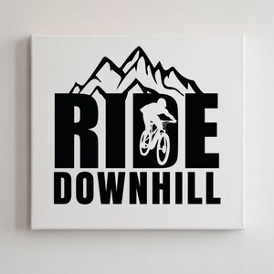 May include: A white canvas print featuring the words "RIDE DOWNHILL" in bold black letters. A silhouette of a mountain biker is integrated into the design, with a mountain range above the word "RIDE".