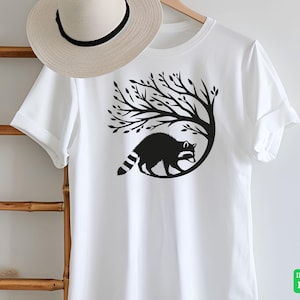May include: White t-shirt featuring a black graphic of a raccoon inside a tree. The raccoon has a striped tail and is surrounded by tree branches. A straw hat hangs on a wooden ladder. The words "INSTANT DIGITAL DOWNLOAD" are in a green box.