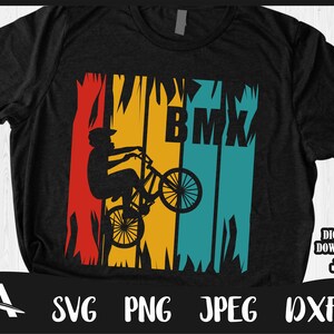 May include: A black t-shirt featuring a retro-style graphic of a person riding a BMX bike. The graphic is in a red, yellow, blue and green colour scheme with the word "BMX" in white letters.