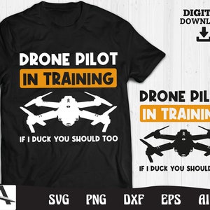 Könnte beinhalten: Schwarzes T-Shirt mit weißem Text, der "Drone Pilot in Training" lautet, und einer weißen Silhouette einer Drohne. Der Text unter der Drohne lautet "If I duck you should too".