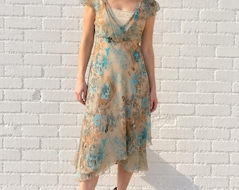 May include: A midi-length dress featuring a tan base with a blue and brown floral pattern, short flutter sleeves, a V-neckline, and a layered hemline. The dress is paired with dark brown leather ankle boots with a pointed toe and block heel.