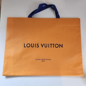 May include: An orange shopping bag with blue handles. The bag features the words "LOUIS VUITTON" in black, with "MAISON FONDÉE EN 1854 PARIS" printed below. The bag is made of paper.