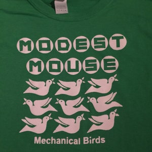 May include: Green t-shirt with a white graphic of the band "Modest Mouse" with the words "Mechanical Birds" printed below. The band name is in a circle font and the birds are stylized.