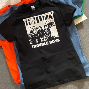 Op de afbeelding: Zwart T-shirt met een witte print van de band Thin Lizzy en de tekst "Trouble Boys".