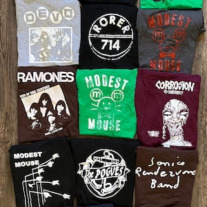 May include: A collection of 12 vintage band t-shirts featuring various bands, including Radio Birdman, The Velvet Underground, Devo, The Cramps, The Pogues, Sonic Rendezvous Band, Corrosion of Conformity, and Modest Mouse.
