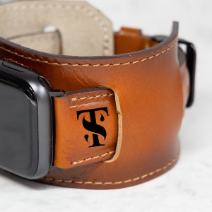 May include: A brown leather watch band with a black monogram of the letters "TS" on the strap.