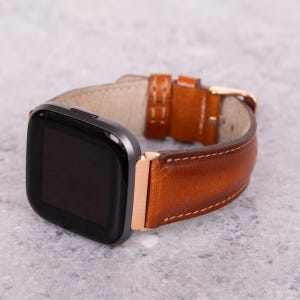 May include: A brown leather watch band with a rose gold buckle and a black smartwatch face.
