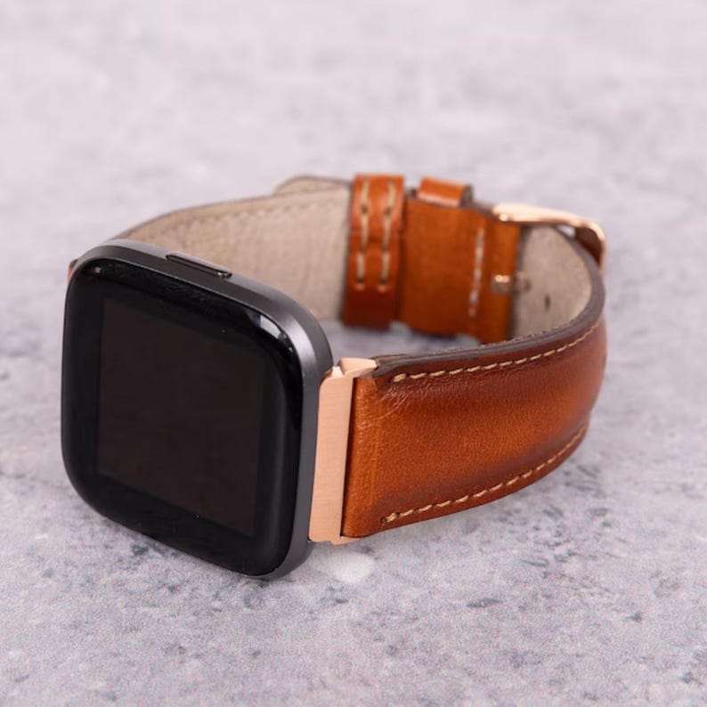 May include: A brown leather watch band with a rose gold buckle and a black smartwatch face.