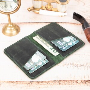 Peut inclure: Un portefeuille en cuir vert avec plusieurs emplacements pour cartes et une poche pour l'argent liquide. Le portefeuille est ouvert et contient des cartes de cr&eacute;dit et des billets en euros.