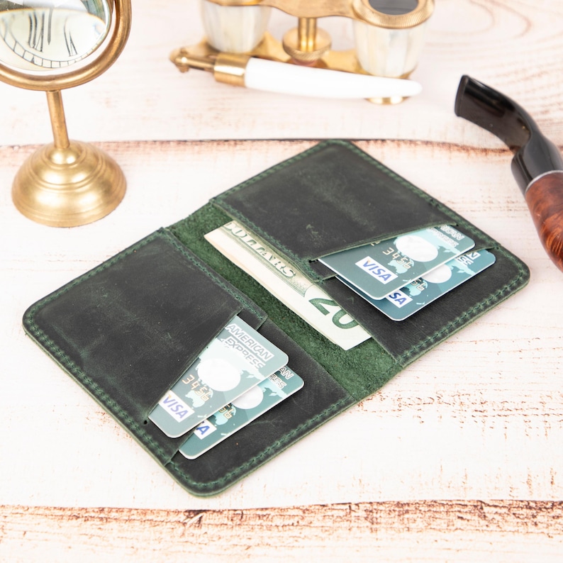 Peut inclure: Un portefeuille en cuir vert avec plusieurs emplacements pour cartes et une poche pour l'argent liquide. Le portefeuille est ouvert et contient des cartes de cr&eacute;dit et des billets en euros.