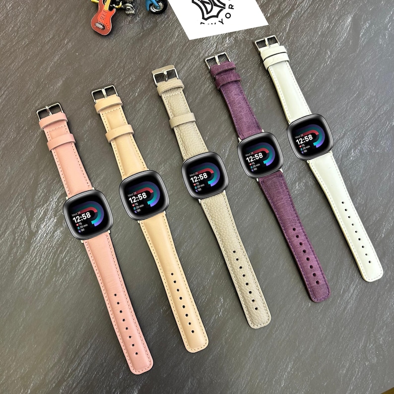 May include: Five different colored leather watch bands for a smartwatch. The bands are in pink, beige, light brown, purple, and white. The watch face displays the time 12:58.