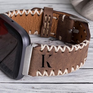 May include: Brown leather watch band with white stitching and a personalized initial "K" engraved on the band.