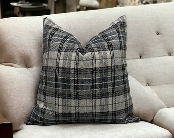 May include: A gray and white plaid throw pillow on a light beige couch. The pillow is made of a soft, textured fabric.