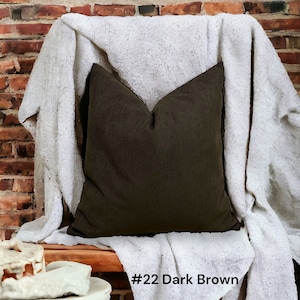 May include: A dark brown throw pillow with a white throw blanket on a wooden bench. The bench is in front of a brick wall. #22 Dark Brown