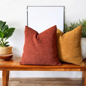 May include: Two throw pillows on a wooden bench. The pillow on the left is a deep red colour and the pillow on the right is a mustard yellow colour.