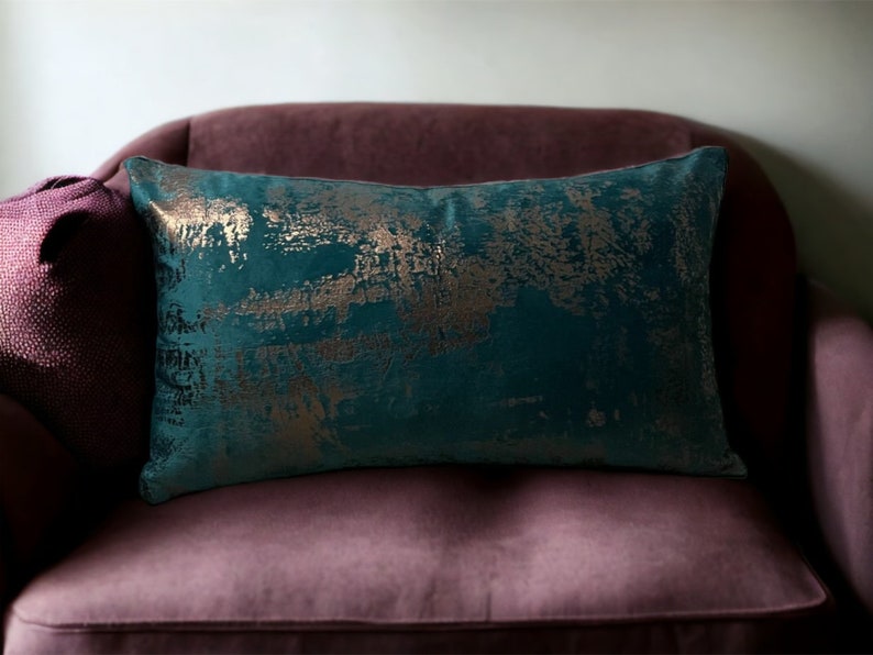 May include: Teal velvet throw pillow with gold metallic accents. The pillow has a distressed, abstract pattern.