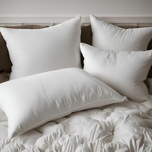 May include: Four white pillows arranged on a white bed with a white duvet cover. The pillows are all different sizes and shapes.