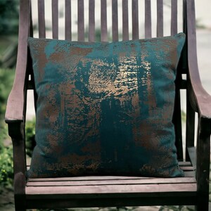 May include: A teal and gold patterned throw pillow on a wooden chair. The pillow has a distressed look with gold accents.