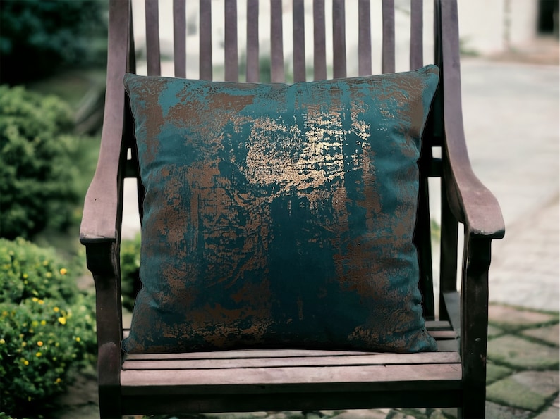 May include: A teal and gold patterned throw pillow on a wooden chair. The pillow has a distressed look with gold accents.