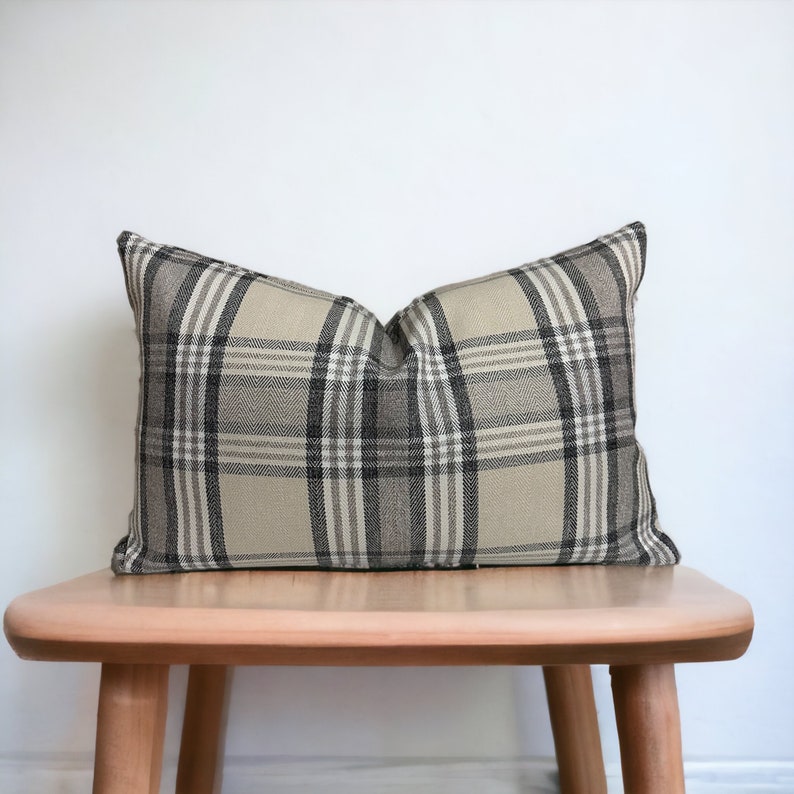 May include: A beige and black plaid throw pillow sits on a wooden stool. The pillow is made of a soft, woven fabric with a subtle sheen.