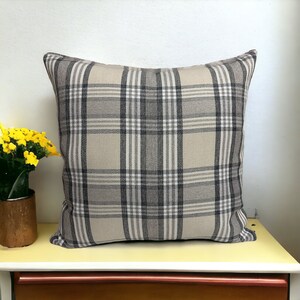 May include: A beige and gray plaid throw pillow with a square shape. The pillow is made of a soft, woven fabric.