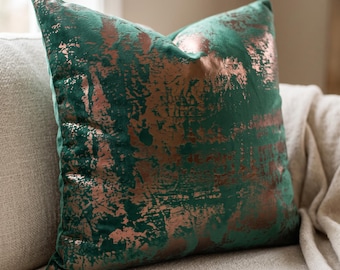 May include: A square throw pillow featuring a deep emerald green velvet fabric base with a metallic copper-colored foil pattern applied in a distressed, abstract, and textured design across the front surface of the cushion cover.