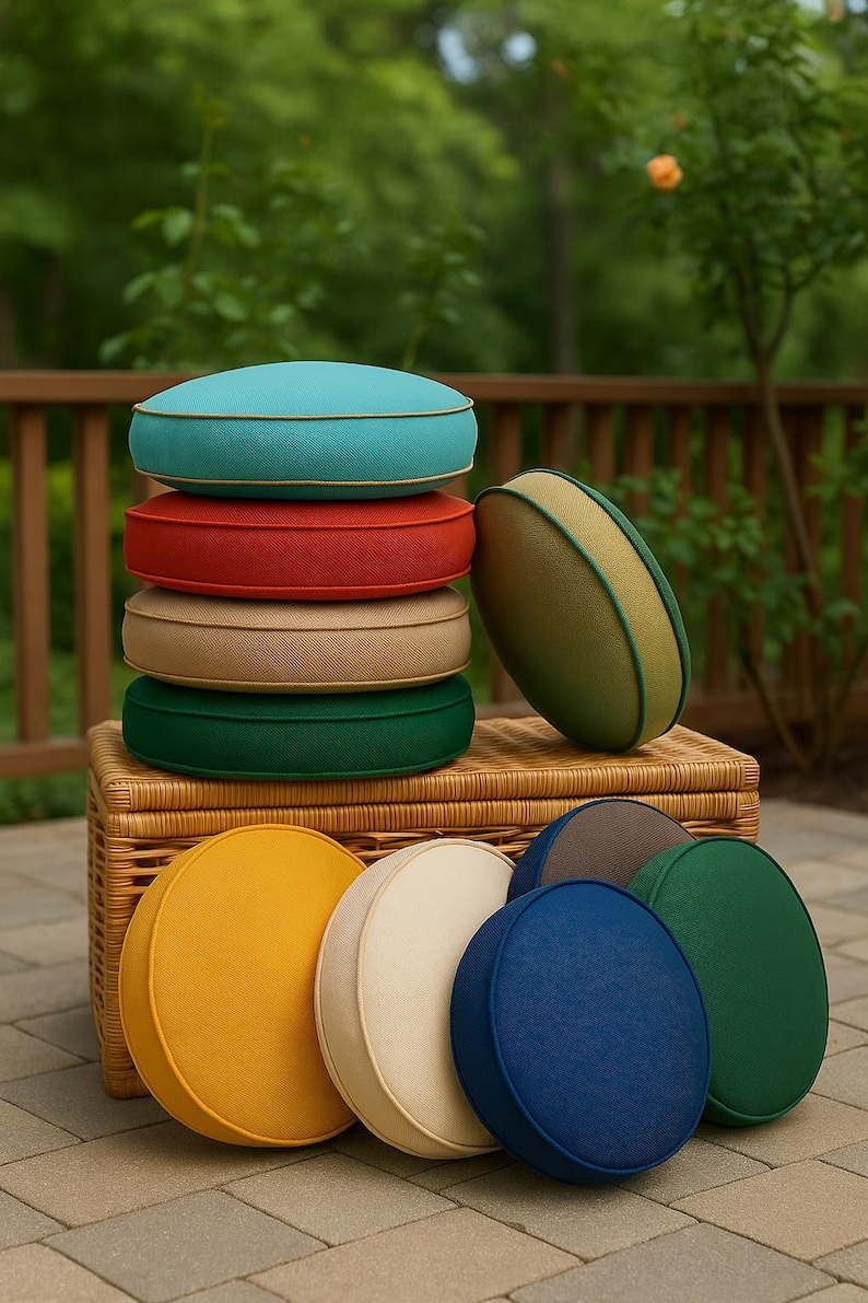 May include: A collection of round, solid-colored cushions featuring piped edges. The stack includes turquoise, red, beige, and dark green cushions, with an olive green one leaning against them. Additional yellow, cream, blue, and green cushions sit below.
