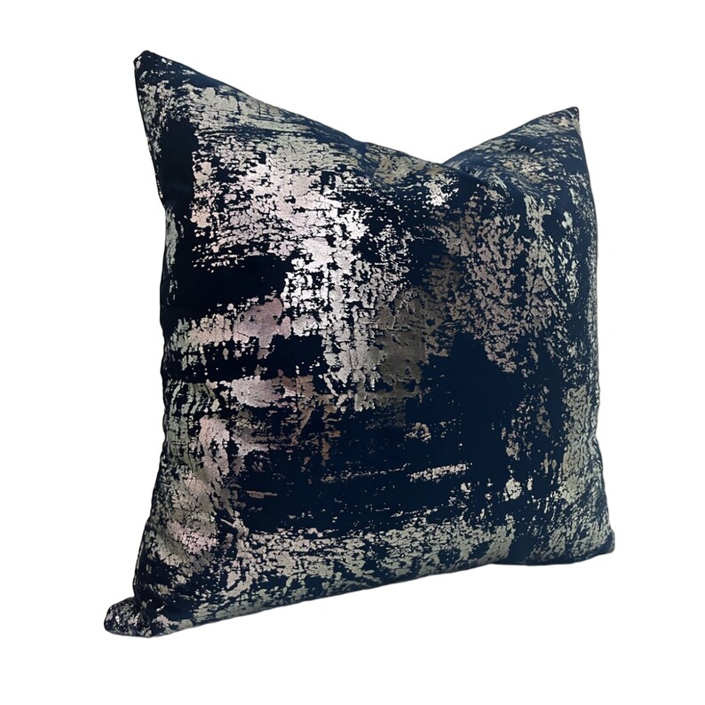 May include: A navy blue throw pillow with a silver metallic abstract design. The pillow is made of a soft, textured fabric.