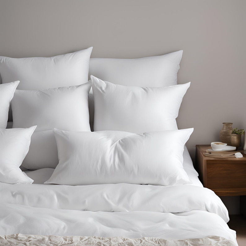 May include: A white bed with a white duvet cover and several white pillows. The bed is made up with a white bedspread and a white throw pillow.
