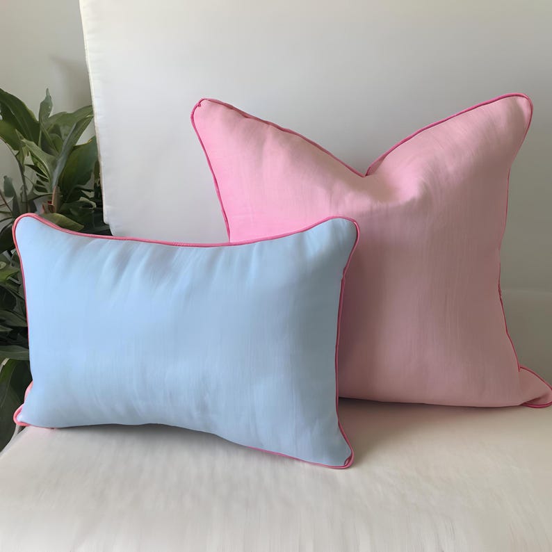 May include: Two decorative throw pillows, one light blue and one pink, with pink piping around the edges.