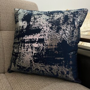 May include: A navy blue throw pillow with a silver abstract design. The pillow is made of a soft, plush fabric and has a subtle sheen.