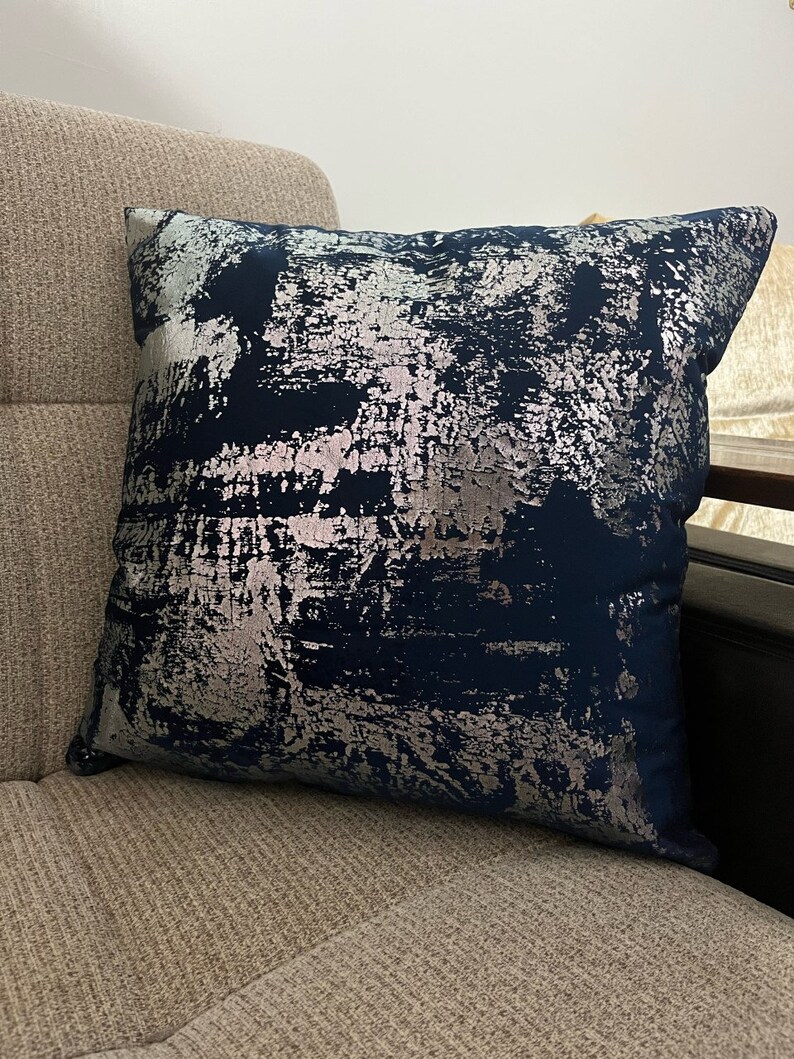 May include: A navy blue throw pillow with a silver abstract design. The pillow is made of a soft, plush fabric and has a subtle sheen.