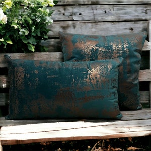 May include: Two teal green throw pillows with a copper metallic distressed pattern. The pillows are on a wooden bench.