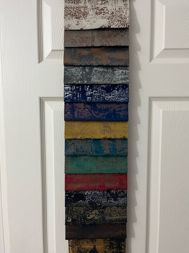 May include: A collection of 15 fabric swatches in various colors and patterns. The swatches are arranged vertically, with the top swatch being a light brown with a white distressed pattern. The swatches below are a variety of colors, including gray, blue, yellow, green, red, black, and brown. Each swatch has a different distressed pattern.