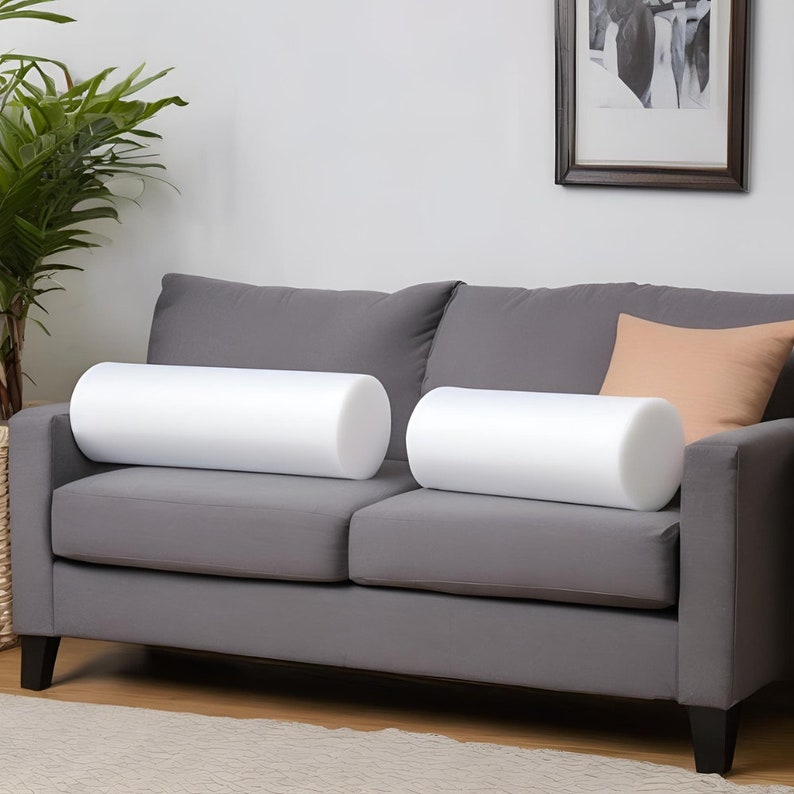 May include: Two white foam cylindrical pillows on a gray sofa with a peach colored throw pillow.
