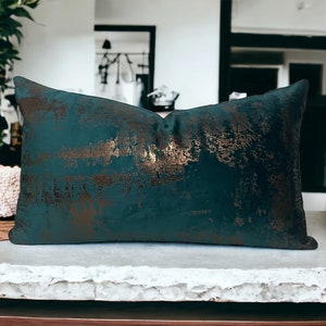 May include: A teal blue throw pillow with a gold metallic pattern. The pillow is made of a soft, plush fabric and has a subtle sheen.