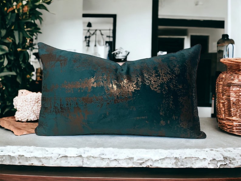 May include: A teal blue throw pillow with a gold metallic pattern. The pillow is made of a soft, plush fabric and has a subtle sheen.