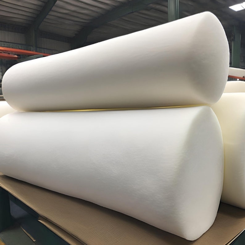 May include: Close-up of white foam rolls stacked on top of each other. The rolls are made of a soft, flexible material and are likely used for upholstery or padding.