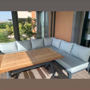 May include: An outdoor sectional sofa with light grey cushions and a rectangular wooden table with a slatted top. The furniture features a dark grey frame and is arranged in an L-shape configuration on a deck with a striped floor pattern.