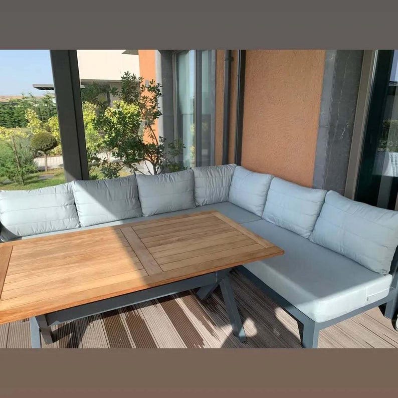 May include: An outdoor sectional sofa with light grey cushions and a rectangular wooden table with a slatted top. The furniture features a dark grey frame and is arranged in an L-shape configuration on a deck with a striped floor pattern.