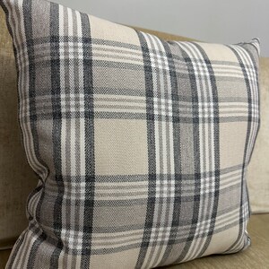 May include: A beige and gray plaid throw pillow with a square shape. The pillow has a subtle herringbone pattern within the plaid.